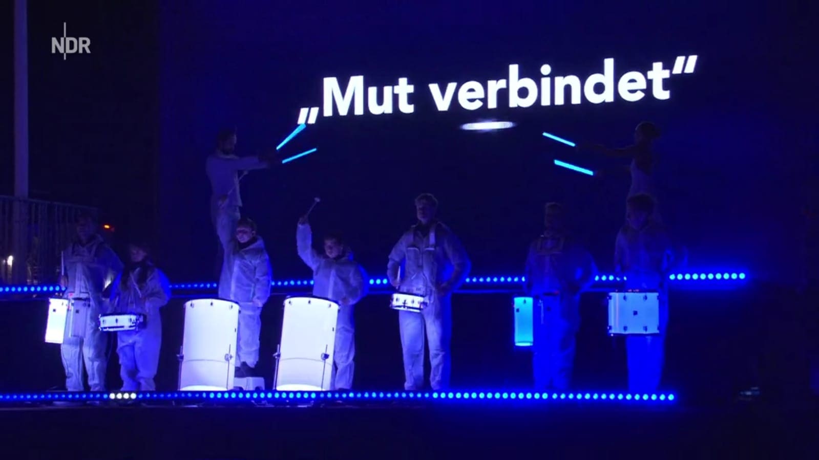 Drumline in blauem Licht auf der Bühne, über ihr der Schriftzug „Mut verbindet“
